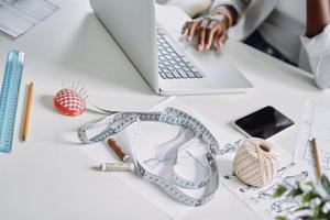 Top view close-up of African woman using laptop while sitting at the desk in fashion design studio photo