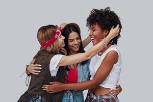 Three attractive stylish young women embracing and laughing while standing against grey background photo