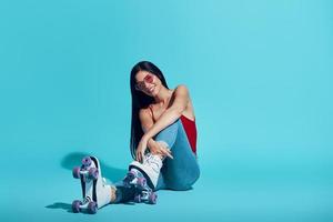 Attractive young woman looking at camera and smiling while wearing roller skates against blue background photo