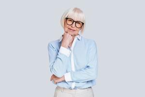 Retirement is a fresh start. Beautiful senior woman looking at camera and smiling while standing against grey background photo