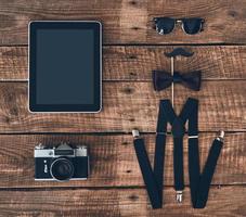 Modern elegance. High angle shot of digital tablet, photo camera, suspenders, prop, bow tie and eyewear lying on wooden desk