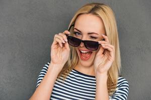 guiño de la belleza. hermosa joven ajustando sus gafas de sol y guiñando un ojo mientras se enfrenta a un fondo gris foto