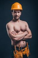 Muscular construction worker. Young confident man keeping arms crossed and looking at camera while standing against black background photo