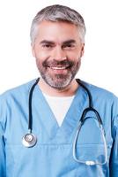 Portrait of confidence and experience. Portrait of happy mature surgeon in blue uniform looking at camera and smiling while standing isolated on white photo