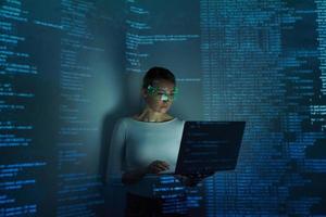 Confident woman in futuristic glasses using computer against dark background photo