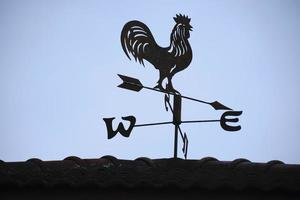 The old wind vane with a rooster symbol icon on the roof, traditional technology equipment for forecast and measuring windy weather in the air, vintage decoration, aiming wind direction instrument. photo