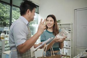 Asian male shopkeeper describes natural organic products to woman customer in refill store, zero-waste and plastic-free grocery, environment-friendly, sustainable lifestyles with reusable containers. photo