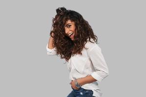 Perfecto en todo sentido. mujer joven atractiva jugando con su cabello y sonriendo mientras está de pie contra el fondo gris foto