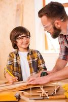 mentes creativas en el trabajo. joven carpintero sonriente y su hijo mirándose mientras trabajan en el taller foto