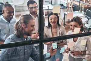 Ensuring success by working as a team. Top view of young modern people in smart casual wear using adhesive notes while standing behind the glass wall in the board room photo