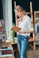 Planning the day. Thoughtful young woman looking in her personal organizer while standing in the workshop photo