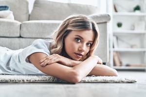 fin de semana de pereza. hermosa joven mirando a la cámara y sonriendo mientras está tirada en el suelo en casa foto