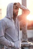 It was intense workout. Side view of tired young man touching his forehead while standing outdoors photo