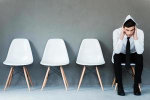 preocupado por la entrevista. joven hombre de negocios frustrado cubriendo su cabeza con papel mientras se sienta en una silla con fondo gris foto