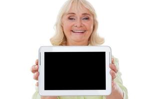 Copy space on her tablet. Cheerful senior woman stretching out digital tablet and smiling while standing isolated on white background photo