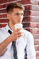 Waiting for inspiration. Handsome young man in shirt and tie holding coffee cup and looking through the window photo