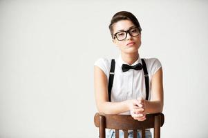 In her own style. Beautiful young short hair woman in white shirt and suspenders sitting on the chair and looking at camera photo