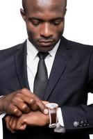 He knows that time is money. Serious young African man in formalwear checking time while looking at his watch and standing isolated on white background photo