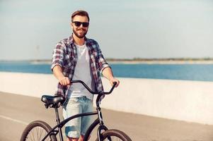 solo yo y mi bicicleta. un joven apuesto parado cerca de su bicicleta y sonriendo mientras está al aire libre foto