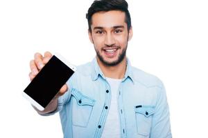 copiar espacio en su teléfono inteligente. joven indio seguro de sí mismo mostrando su teléfono inteligente y sonriendo mientras está de pie contra el fondo blanco foto