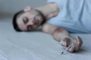 The last injection. Young man lying on the floor and keeping eyes closed while holding syringe in his hand photo