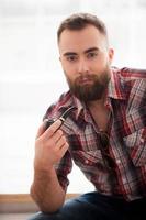 Man with a smoking pipe. Bearded handsome young man holding a smoking pipe and looking at camera while sitting on the chair photo