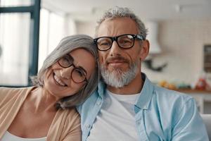Senior couple in casual clothing smiling and looking at camera while spending time at home photo
