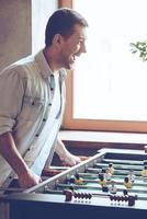 Loving this game. Side view of cheerful young handsome man playing foosball game and looking excited while standing in front of window photo
