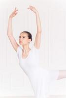 belleza en cada uno de sus movimientos. joven bailarina confiada en tutú blanco manteniendo los brazos levantados mientras baila en el estudio de ballet foto