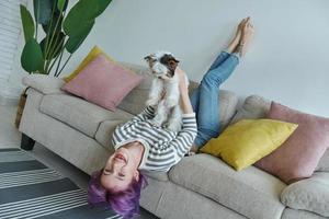 Playful teenage girl carrying her little dog while relaxing on the couch at home photo
