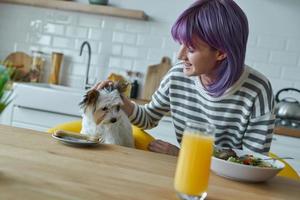 Teenage girl and her little dog having lunch together while sitting at the kitchen island photo