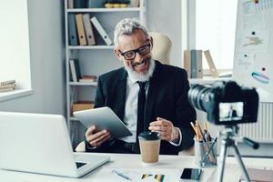 Confident mature man in elegant suit telling something and smiling while making social media video photo