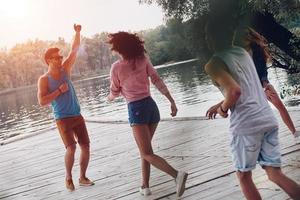 diversión sincera. toda la longitud de los jóvenes en ropa casual sonriendo y divirtiéndose mientras están de pie en el muelle foto