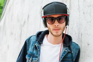 Music is my life. Serious young man in headphones looking at camera while leaning at the concrete wall photo