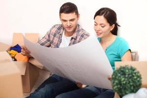 Examining a blueprint. Beautiful young couple sitting on the floor and looking at the blueprint while cardboard boxes laying around them photo