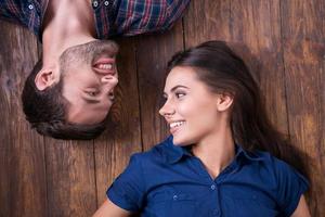 Enjoying closeness. Top view of beautiful young loving couple lying together on the hardwood floor and looking at each other photo