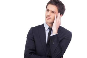 Lost in thoughts. Thoughtful young man in formalwear holding hand in hair and looking away while standing isolated on white background photo