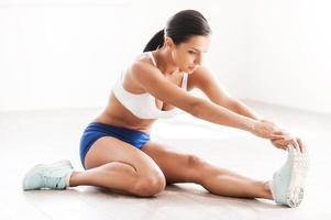 estirar para el éxito. bella joven con ropa deportiva haciendo ejercicios de estiramiento mientras se sienta en el suelo foto