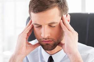 sentirse cansado y deprimido. joven deprimido con camisa y corbata sosteniendo la cabeza en las manos y manteniendo los ojos cerrados mientras se sienta en su lugar de trabajo foto