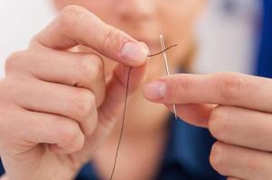 Thread into the needle. Close-up of woman pulling thread into the needle photo