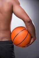 Ready to play. Rear view of shirtless African man holding basketball ball while standing against grey background photo