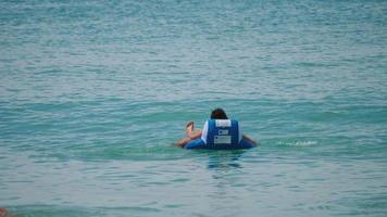 phuket, tailandia 20 de noviembre de 2018 - vista trasera, un hombre flota en un anillo de natación inflable en el mar azul. concepto de turismo y viajes video