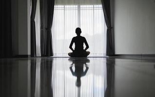 Silhouette of young woman meditating at home. Men practicing yoga indoors. Relaxation, body care, meditation, balance, fitness,  workout, recreation concept,  pray. photo