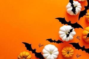 Halloween flat lay composition of black paper bats fand pumpkins on orange background. Halloween concept. photo