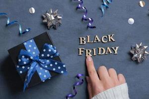 Black Friday text and female hand with gift and holiday tinsel flat lay flat lay on dark cement background. Top view photo