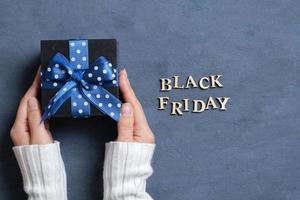 Black Friday text with gift in female hands flat lay on dark cement background. Top view photo