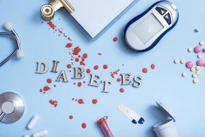 palabra diabetes con jeringa de insulina, lanceta, prueba, medidor de glucosa sobre fondo azul foto