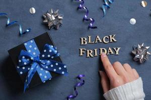 Black Friday text and female hand with gift and holiday tinsel flat lay flat lay on dark cement background. Top view photo