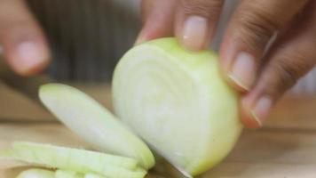 Close up of hands cutting onions with knife on wooden Cutting board