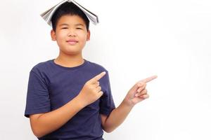 A picture of a boy in glasses point to the side and covering his head with a book. Education and learning concept. photo